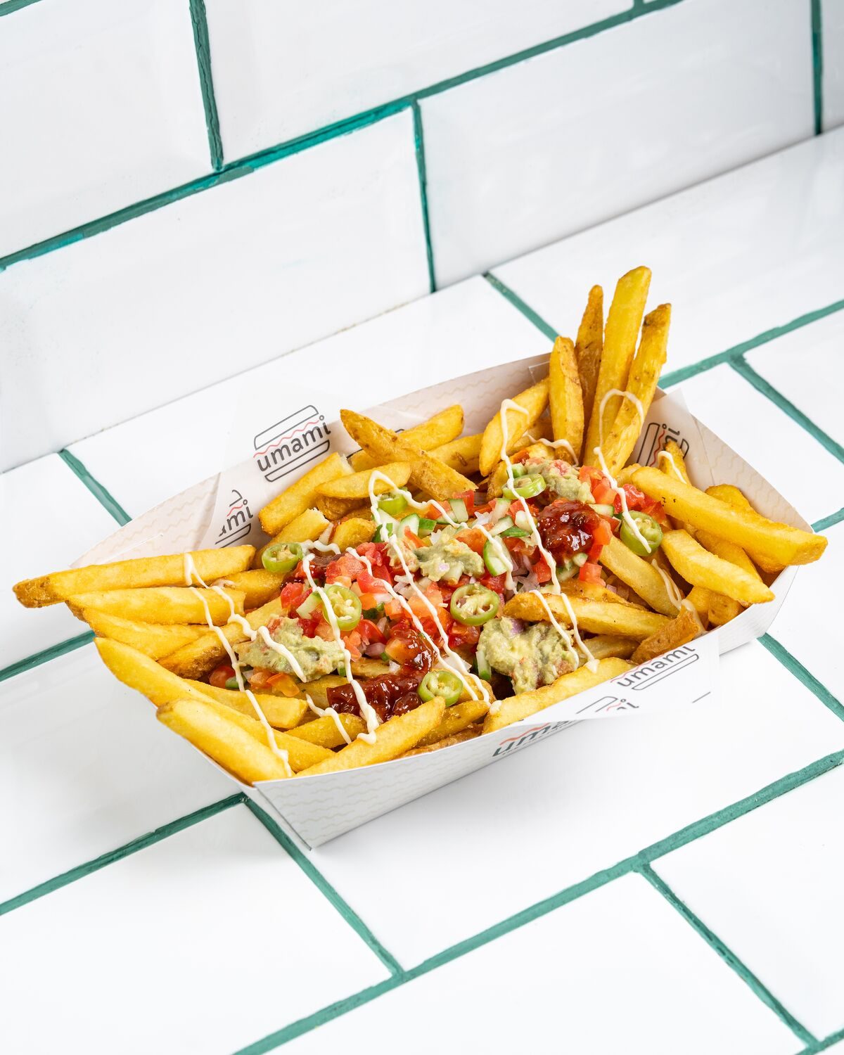 Fries loaded with fresh tomato salsa, green avocado sauce, a white cream drizzle and sliced jalapenos, shot at a forty five degree angle.