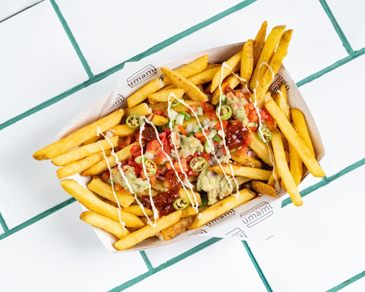 Fries loaded with fresh tomato salsa, green avocado sauce, a white cream drizzle and sliced jalapenos, shot from directly overhead.