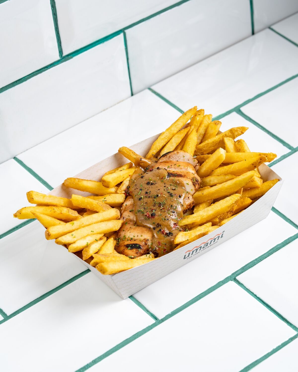 A tray of seasoned fries topped with a grilled steak fillet and a peppered cream gravy flecked with herbs, shot at a forty five degree angle.