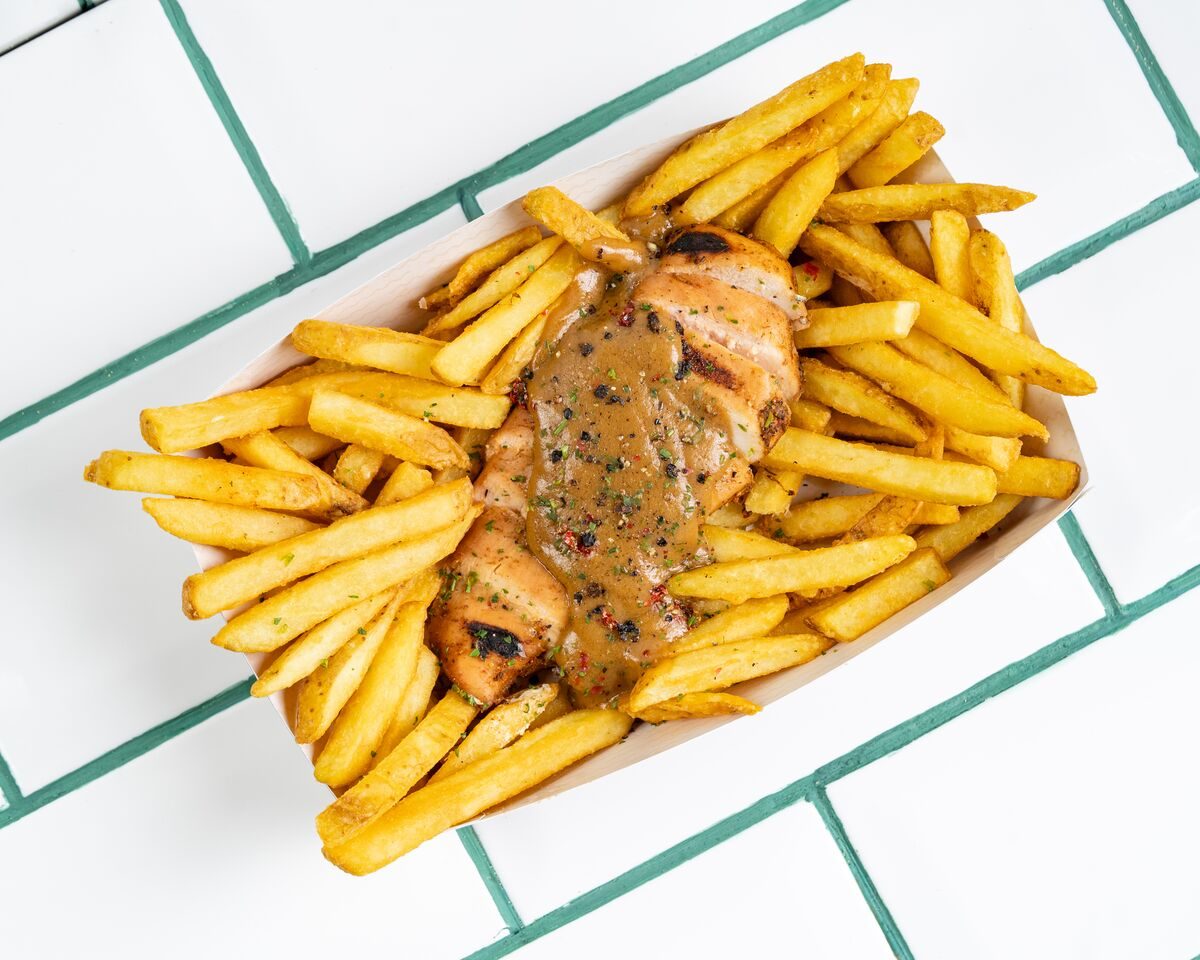 A tray of seasoned fries topped with a grilled steak fillet and a peppered cream gravy flecked with herbs, shot from directly overhead.