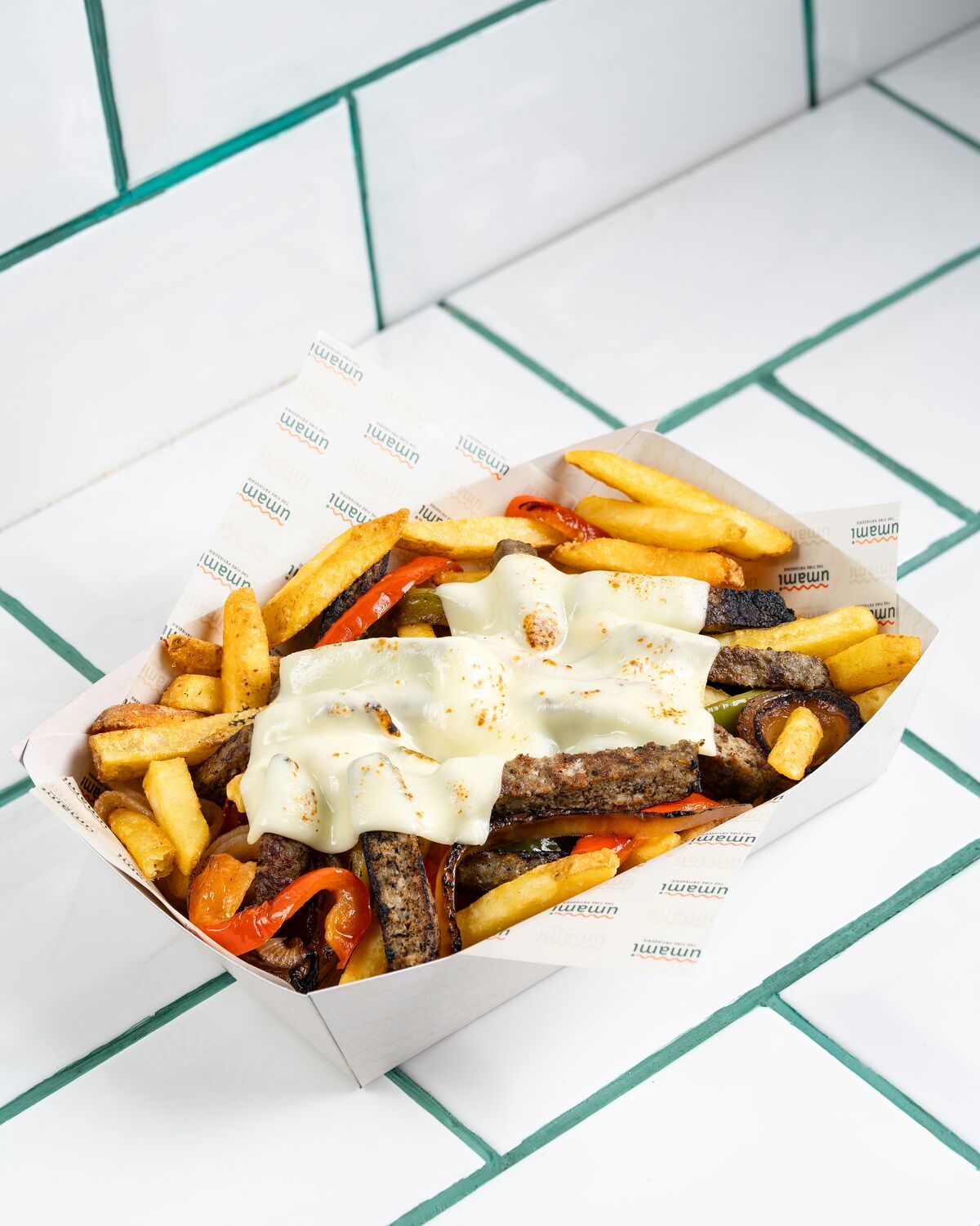 Fries piled with strips of grilled meat and red and yellow peppers under slices of melted white cheese, shot at a forty five degree angle.
